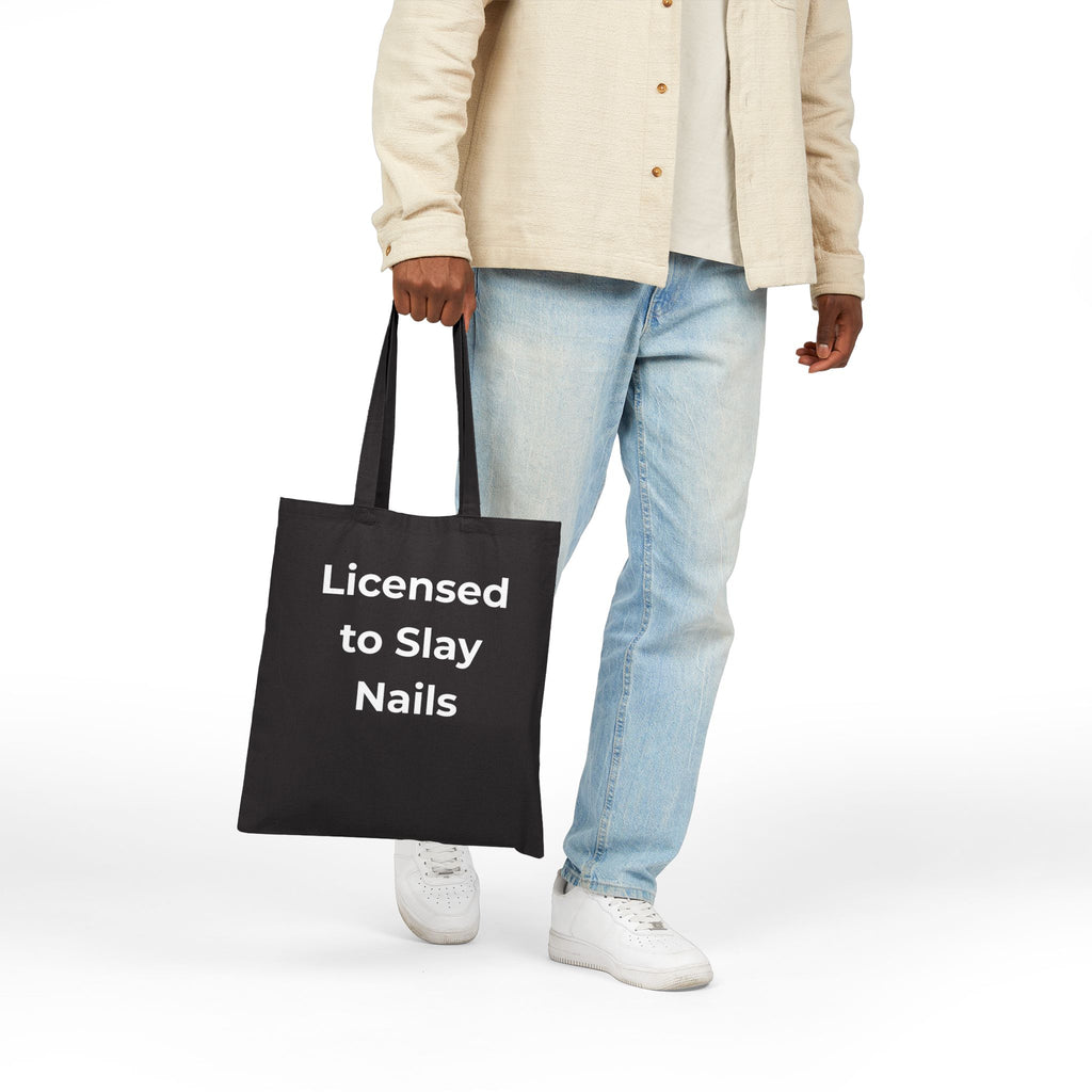 Person holding a black tote bag with 'Licensed to Slay Nails' text on a white background