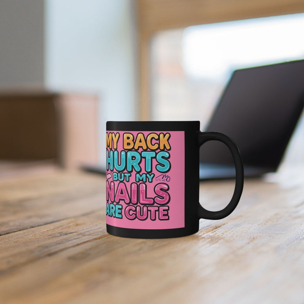 Black mug with colorful text on a pink background, placed on a wooden surface.