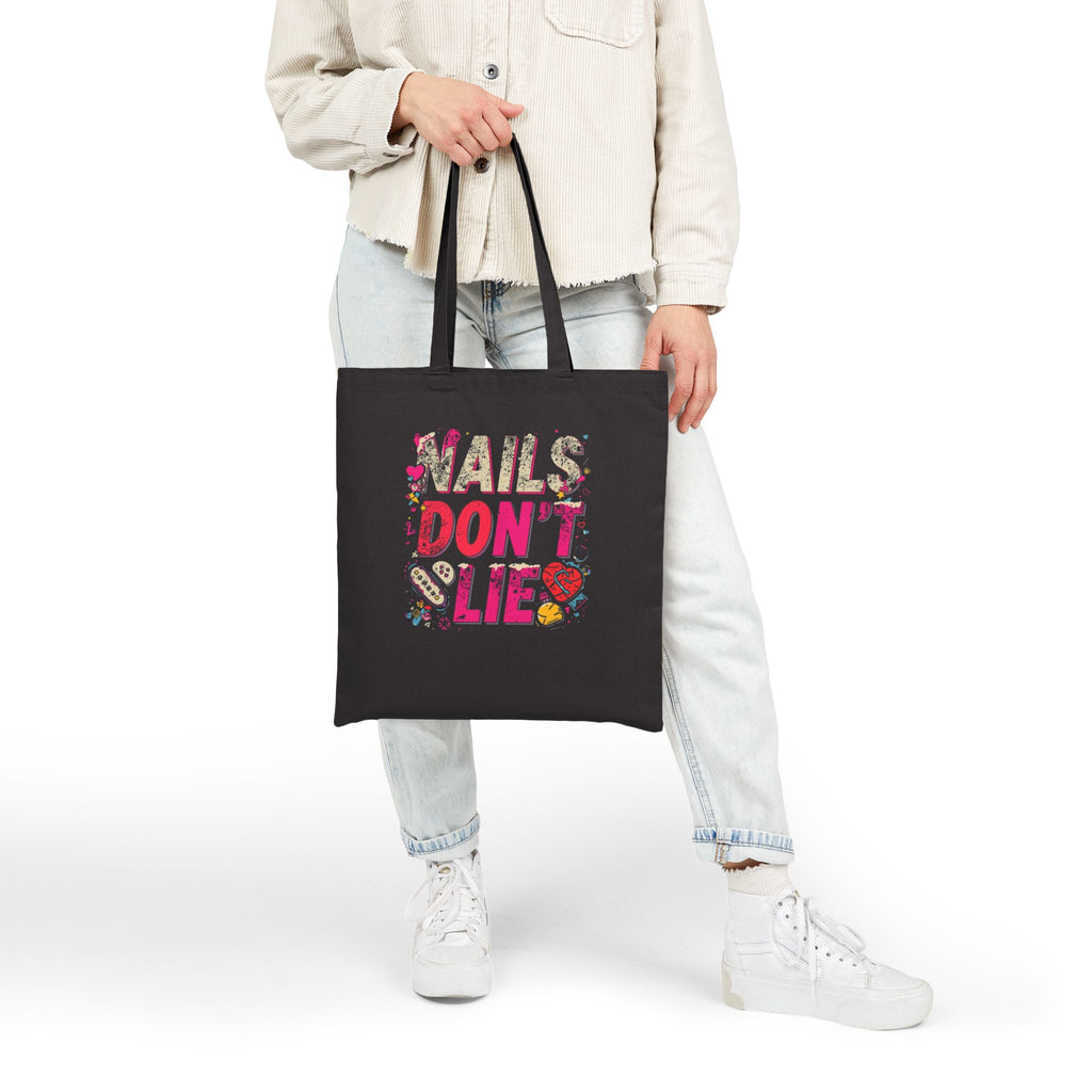 Person holding a black tote bag with 'Nails Don't Lie' text and graphics.