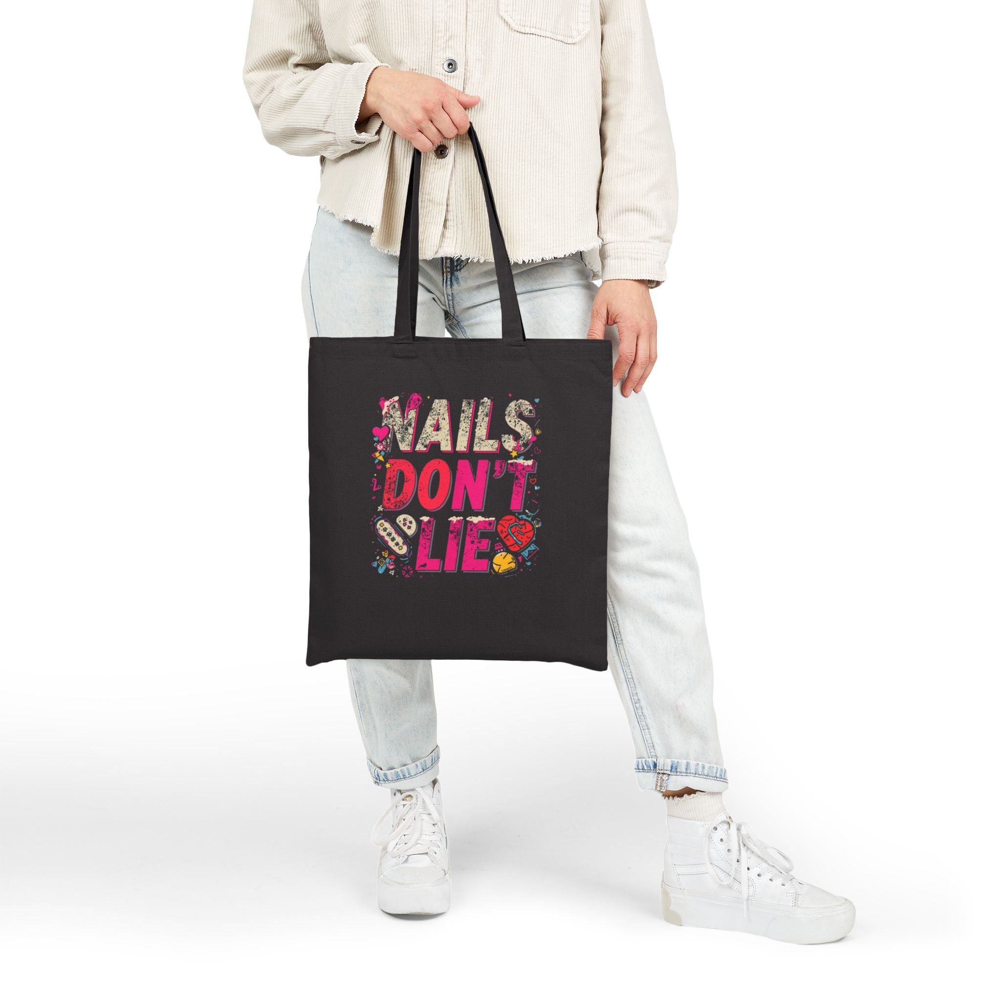 Person holding a black tote bag with 'Nails Don't Lie' text and graphics.